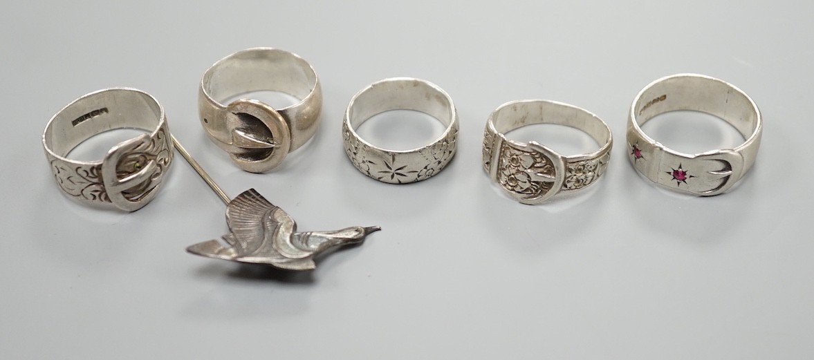 Four assorted silver buckle rings, including one set with red stones, an engraved silver band and a 925 duck stick pin.